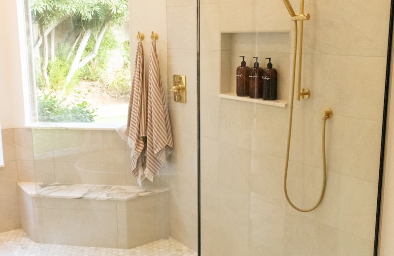 Glass-enclosed shower with brushed gold fixtures and penny tile flooring