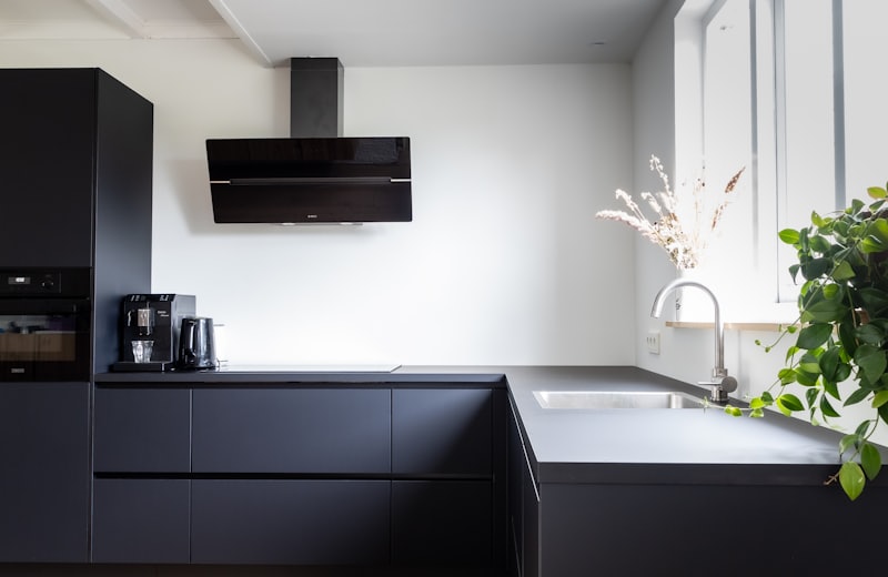 Matte black minimalist kitchen with wood flooring and a hooded range