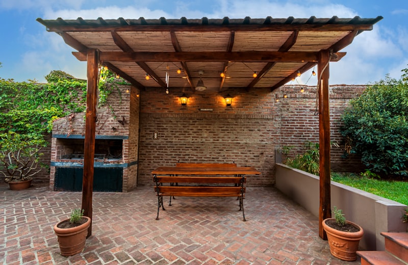 Covered brick pergola with a wood dining table and string lights